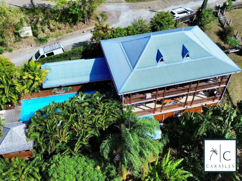 Belle maison avec une grande terrasse et une piscine, entourée d'une végétation luxuriante.