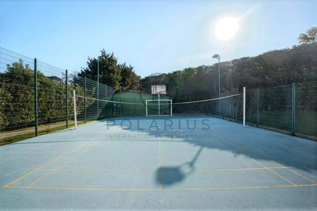 Terrain de sport polyvalent au soleil, entouré de clôtures et de verdure.