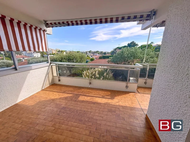 Une terrasse avec un sol en carreaux brun, des auvents rayés, et une vue dégagée sur la nature environnante.