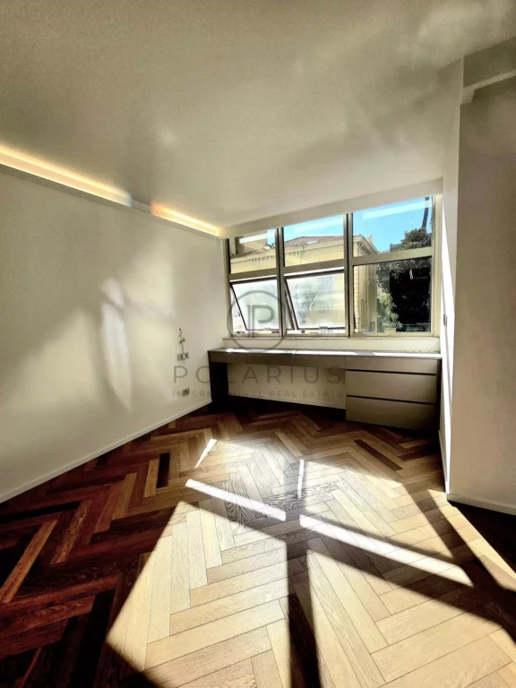 Une pièce lumineuse avec un sol en bois à chevrons et une grande fenêtre en angle.