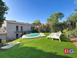 Grande maison avec jardin, piscine et chaises longues sous un ciel bleu.