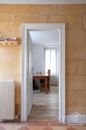 Un couloir avec un mur en pierre mène à une pièce lumineuse avec une table en bois.