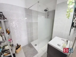 Une salle de bain moderne avec une douche à l'italienne, un évier blanc et une étagère contenant divers articles.