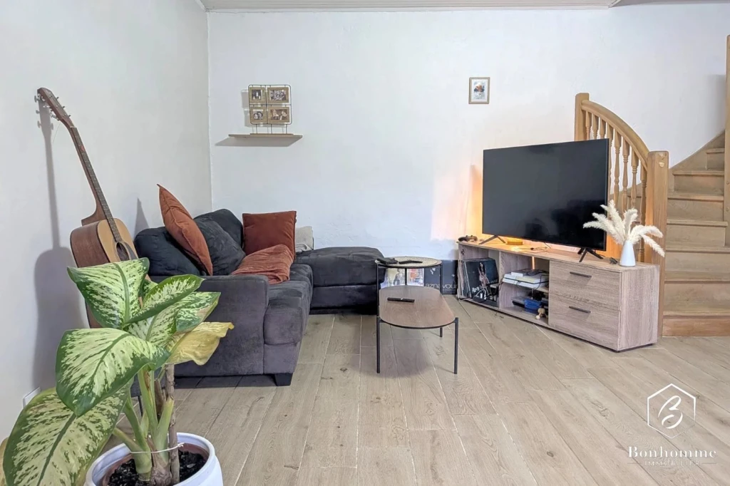 Salon lumineux avec canapé confortable et vue sur l'escalier en bois.