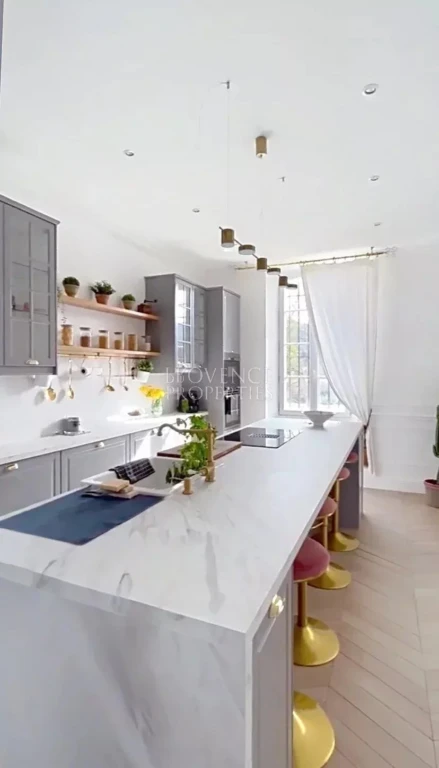 Vue d'ensemble de la cuisine baignée de lumière, avec son grand îlot central dînatoire parfait pour les moments en famille ou entre amis.