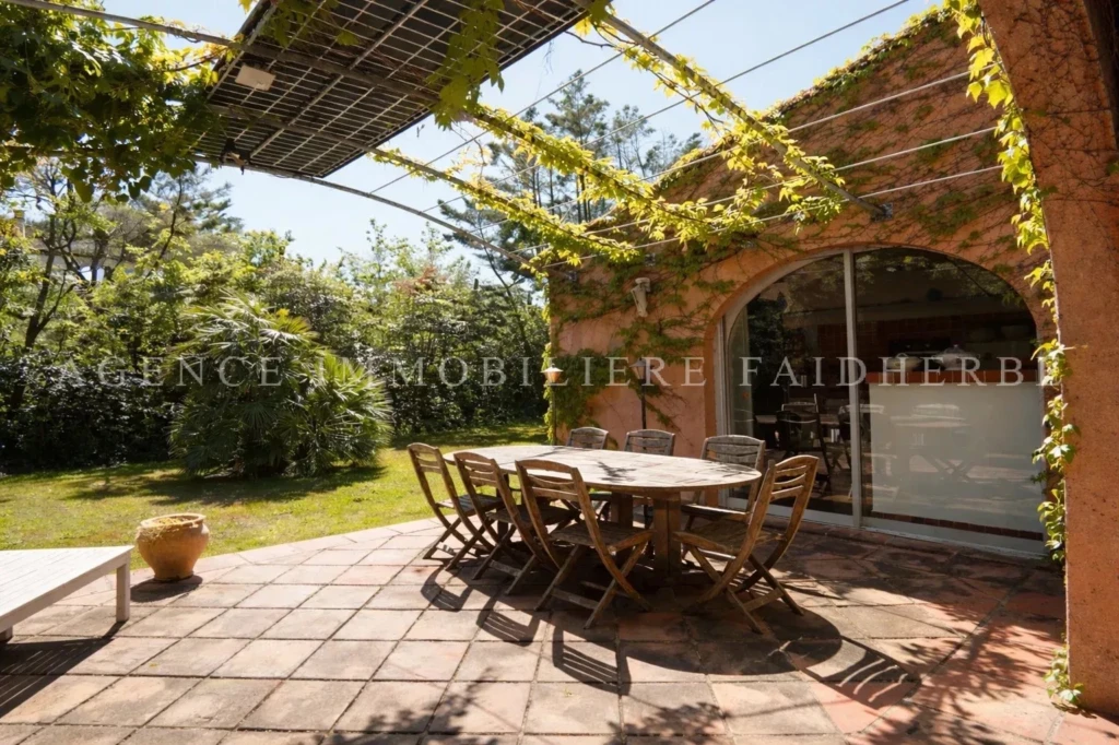 Terrasse ensoleillée avec un espace pour manger et un jardin verdoyant.