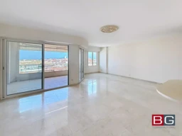 Une pièce lumineuse avec un sol en marbre et de grandes baies vitrées offrant une vue sur la mer.