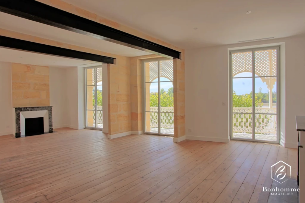 Un salon lumineux avec parquet en bois clair, équipé d'une cheminée, et de grandes fenêtres donnant sur un balcon.