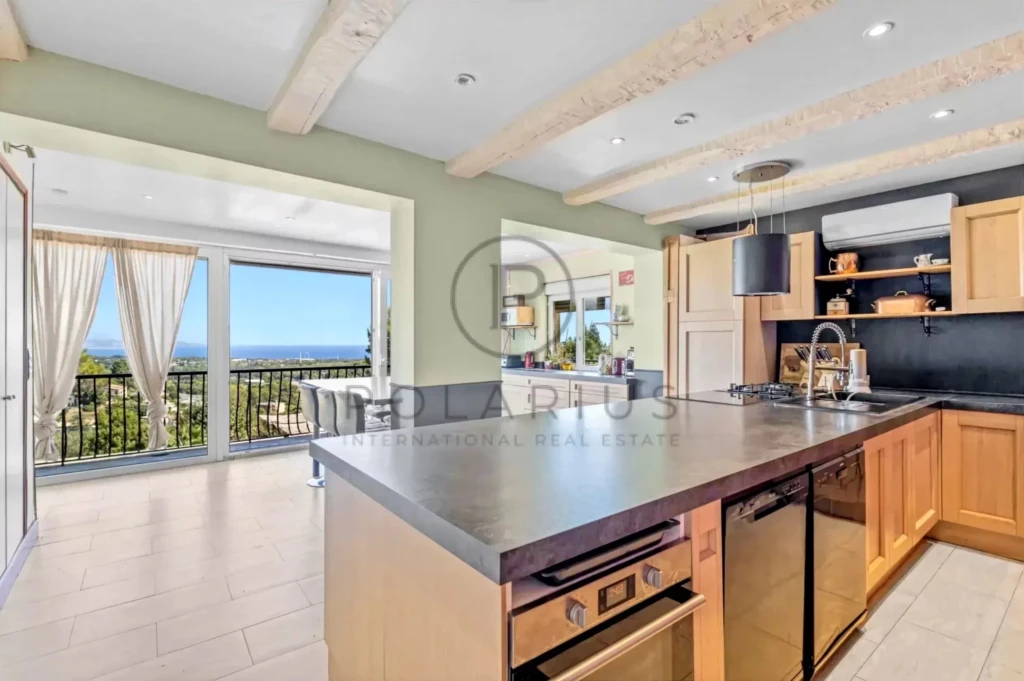 Cuisine moderne avec un îlot central en bois, ouverte sur un salon lumineux avec vue sur la mer.