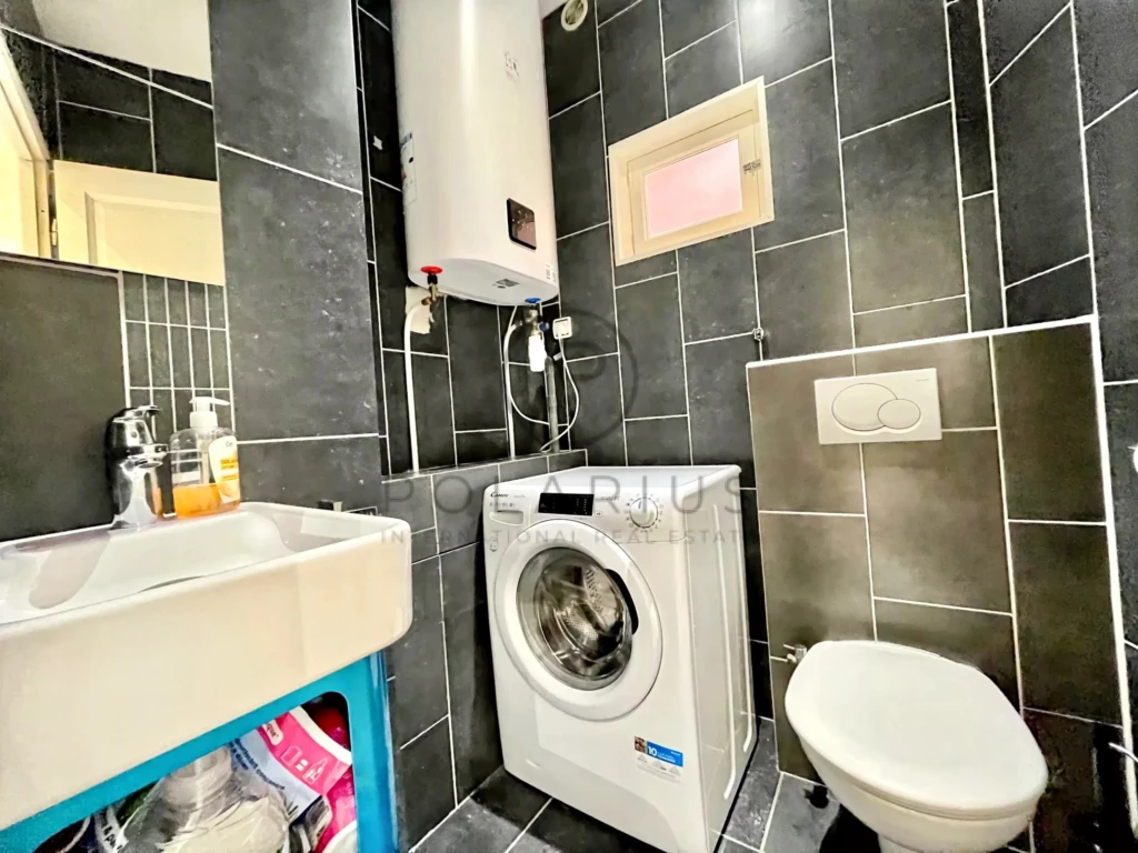 Petite salle de bain avec lave-linge, lavabo et toilette dans un espace moderne et fonctionnel.
