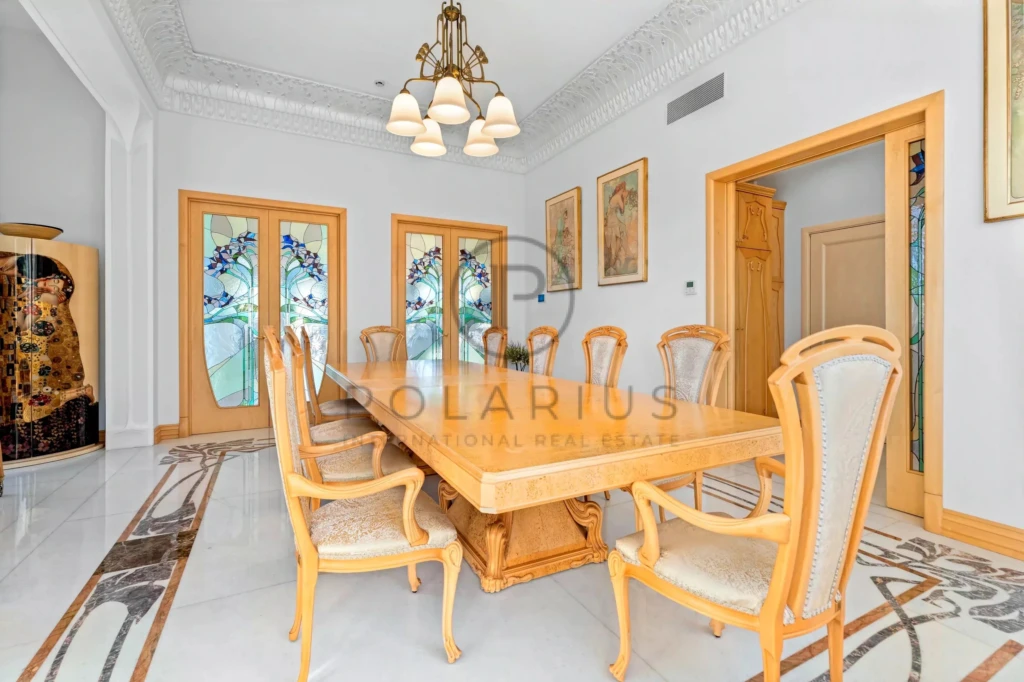 Une salle à manger élégante avec une grande table en bois entourée de chaises, des portes avec des vitraux colorés et un lustre classique.