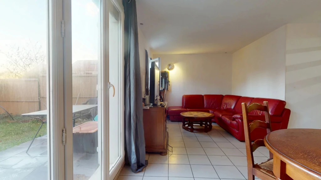 Un salon avec un canapé rouge, une télévision, une table en bois, et une porte vitrée donnant sur l'extérieur.