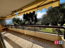 Une terrasse spacieuse avec un auvent jaune surplombe un jardin verdoyant, offrant une vue dégagée sur les arbres environnants.