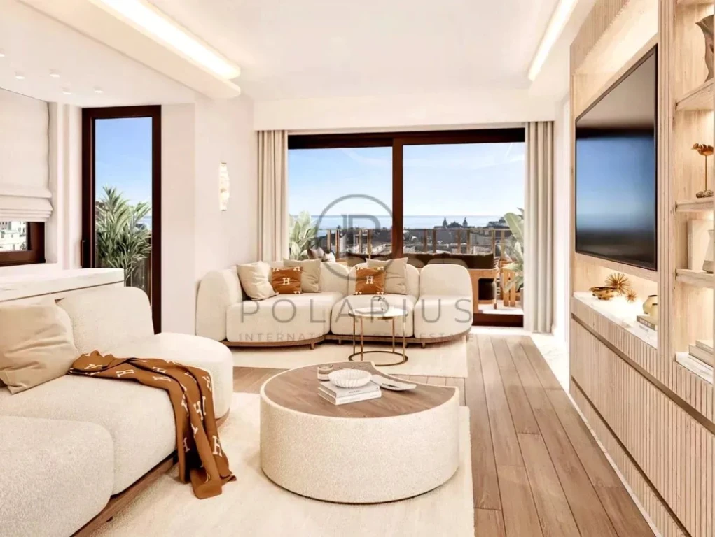 Un salon élégant avec des meubles modernes en crème, un grand téléviseur, et une vue sur la mer à travers de grandes fenêtres.