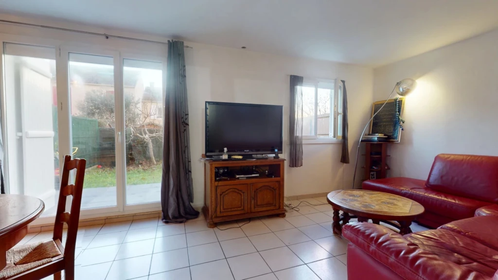Un salon lumineux avec des canapés en cuir rouge, une télévision sur un meuble en bois, et une grande fenêtre donnant sur le jardin.
