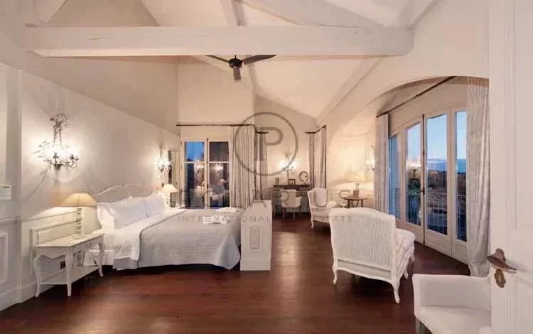 Une chambre élégante avec un plafond en bois, un grand lit, des fauteuils, et des fenêtres offrant une belle vue extérieure.