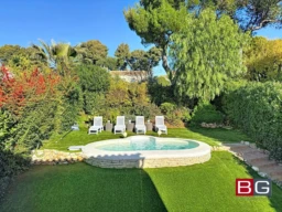 Un jardin verdoyant avec une petite piscine entourée de quatre chaises longues sous un ciel bleu.