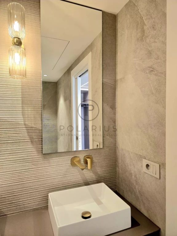 Un lavabo moderne avec un robinet doré, un grand miroir et des murs texturés dans une salle de bain.
