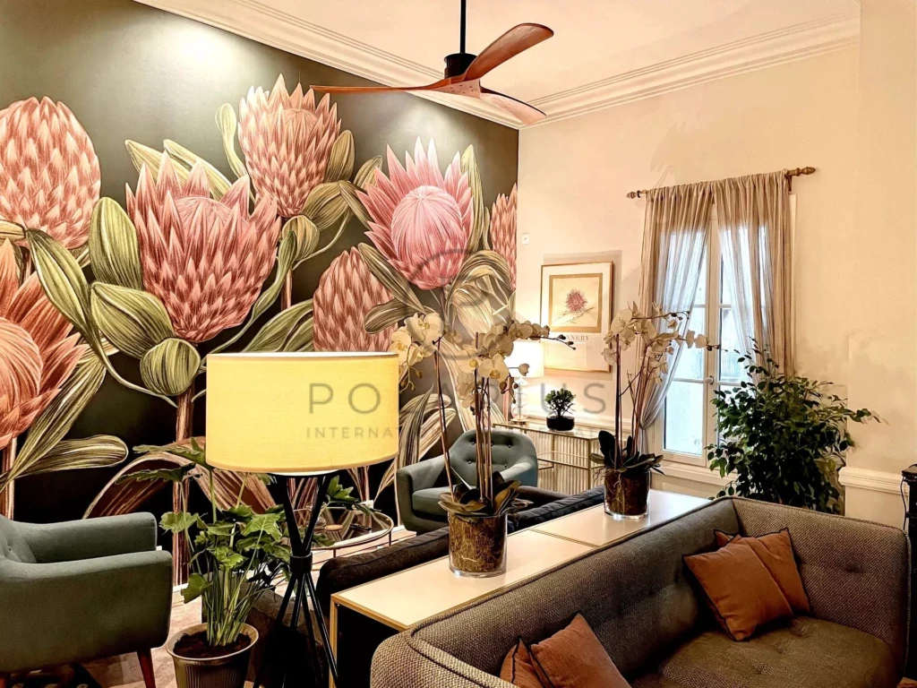 Un salon élégant avec un grand mur décoré de fleurs roses et des meubles confortables, incluant des plantes et des lampes.