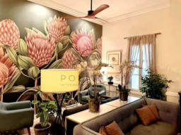 Un salon élégant avec un grand mur décoré de fleurs roses et des meubles confortables, incluant des plantes et des lampes.