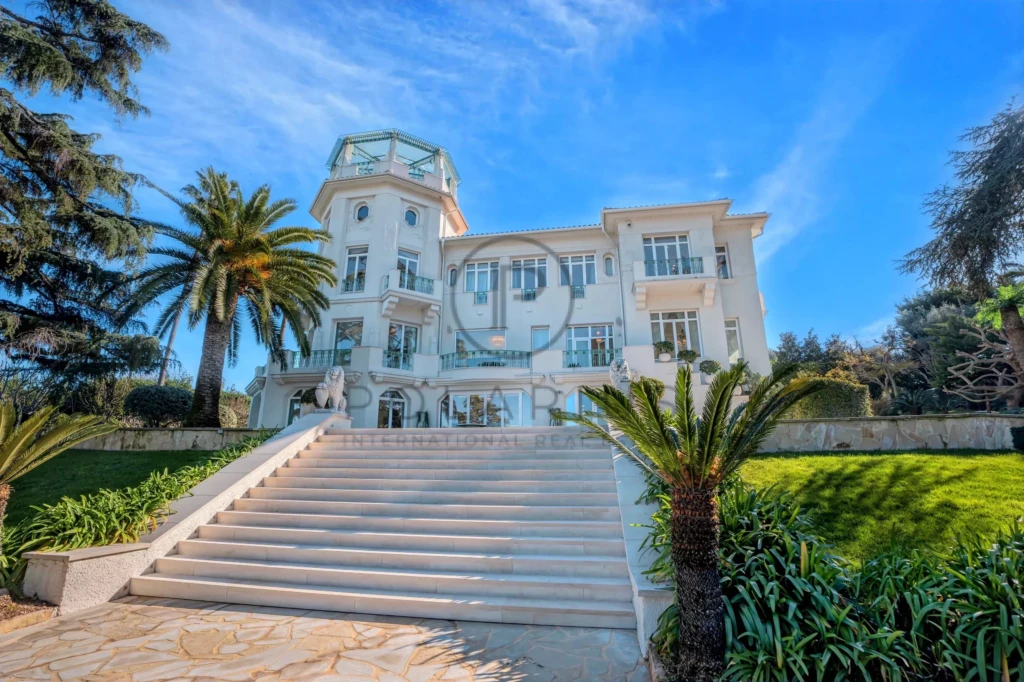 Une villa élégante avec un escalier en marbre et des palmiers, sous un ciel bleu éclatant.