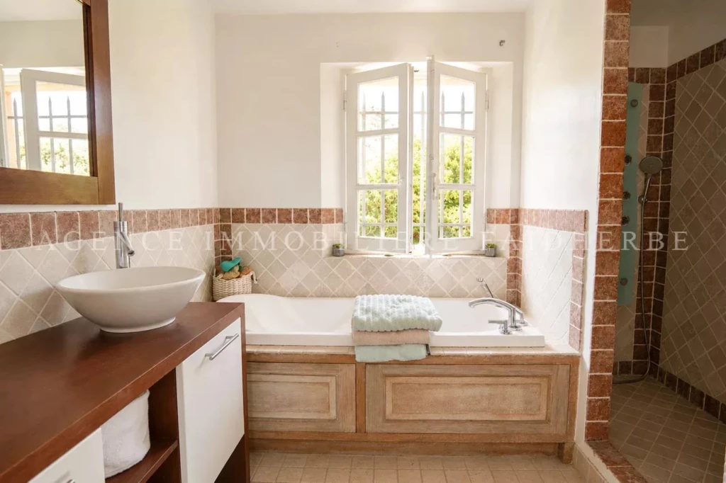 Belle salle de bain avec baignoire, lavabo sur meuble et douche séparée, lumineuse grâce à une grande fenêtre.