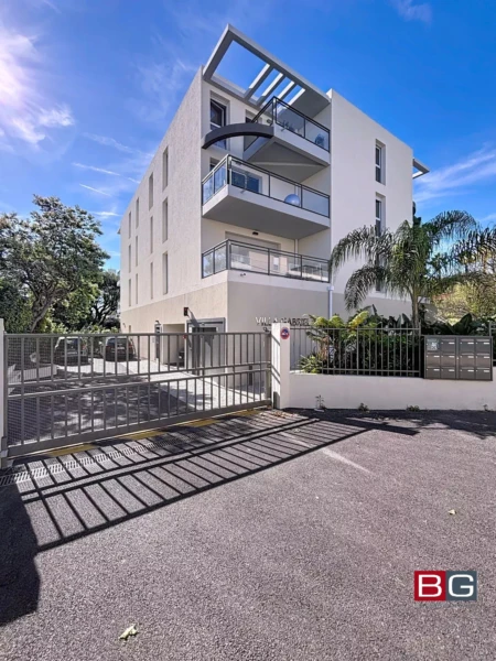 Un immeuble moderne avec balcons, entouré de végétation, sous un ciel bleu.