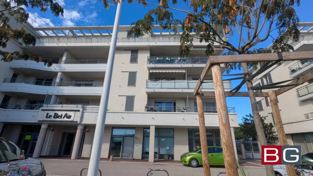 Un immeuble moderne avec des balcons et une voiture verte garée devant, sous un ciel bleu.