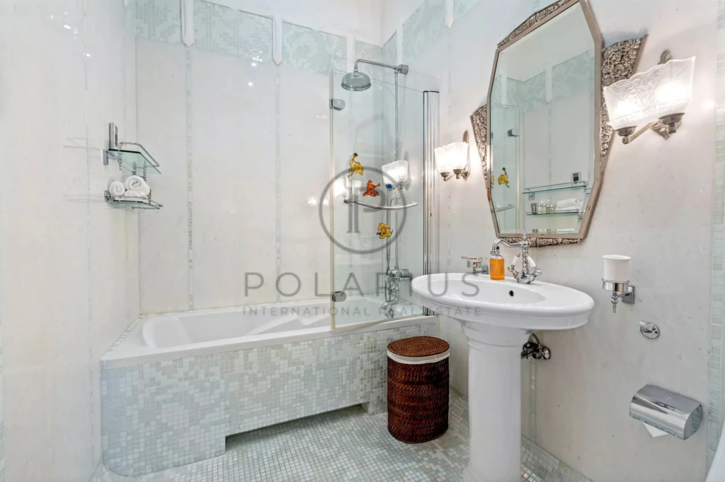 Salle de bain élégante avec baignoire, miroir octogonal, et lavabo sur pied.