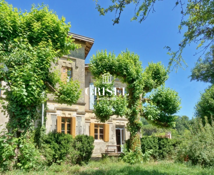 Une maison en pierre entourée de verdure et d'arbres sous un ciel bleu.