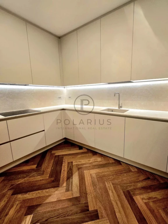 Cuisine moderne avec des armoires blanches, un évier en inox et un parquet en bois foncé disposé en chevrons.