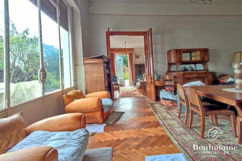 Salon lumineux avec parquet, meubles en bois et grande fenêtre donnant sur la verdure.