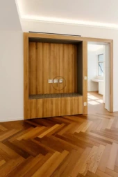 Un intérieur moderne avec parquet en bois et une niche murale, illuminé par une lumière naturelle provenant d'une pièce adjacente.