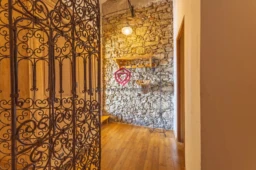 Un couloir chaleureux avec un mur en pierre apparente, un sol en bois, et une porte ornée de fer forgé.
