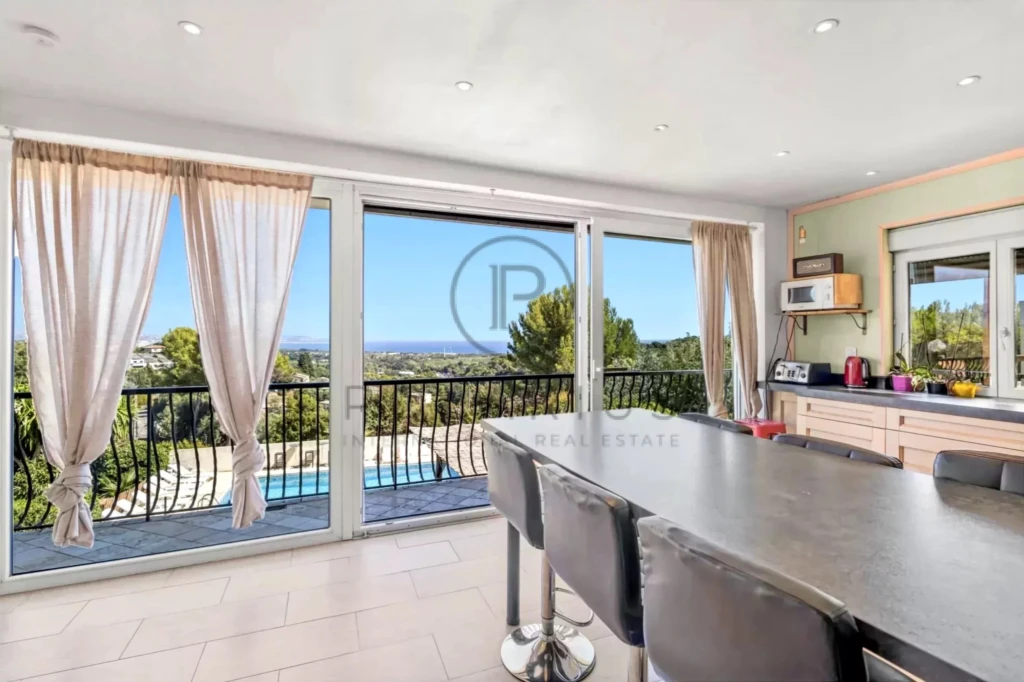 Cuisine moderne avec vue sur piscine et paysage, dotée de grandes baies vitrées et d'une table à manger.