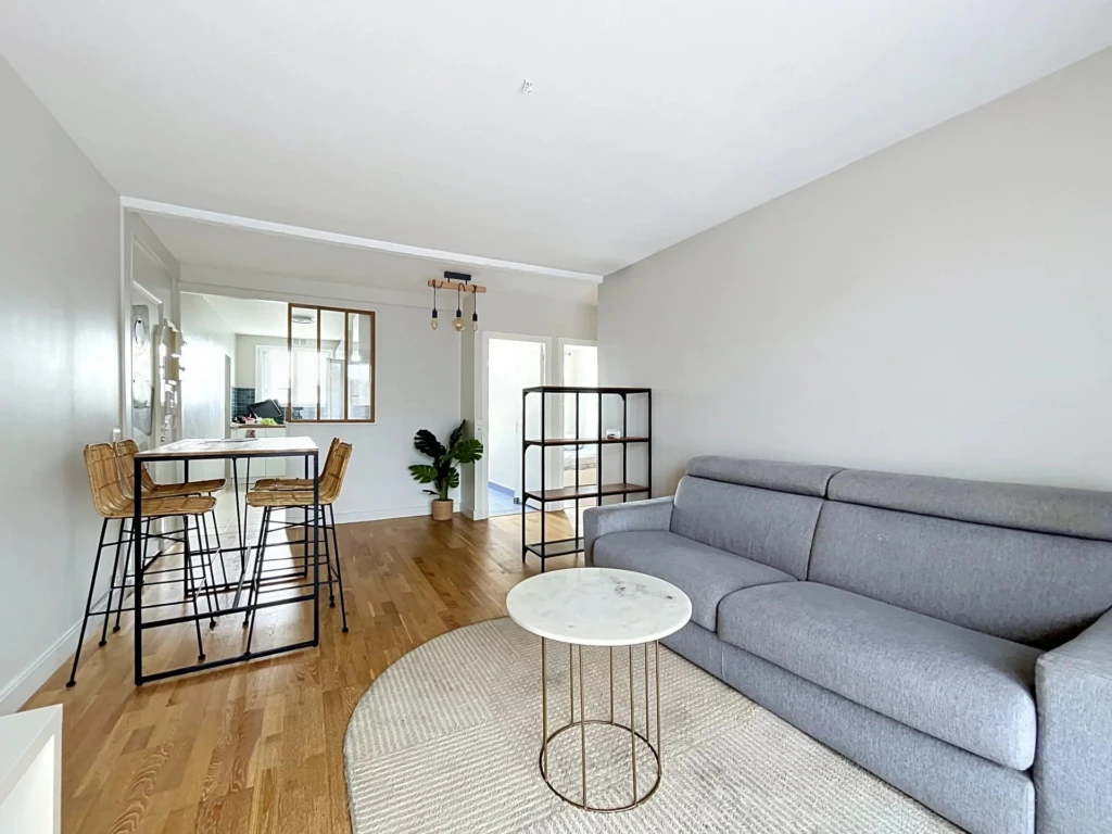 Un salon lumineux avec un canapé gris, un tapis rond et une table basse élégante.