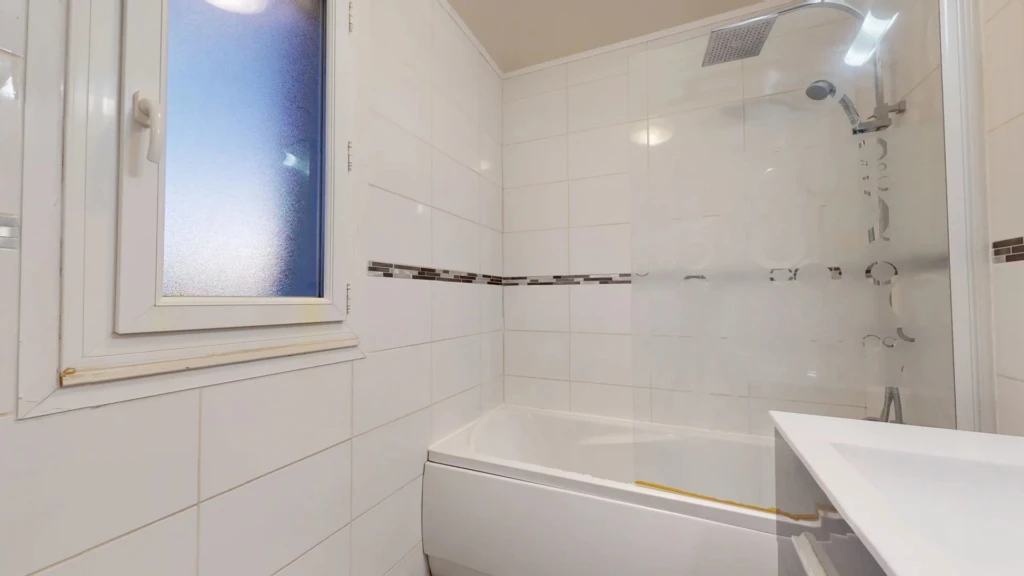 Une salle de bain moderne avec une baignoire et une douche intégrée, des murs carrelés et une fenêtre.