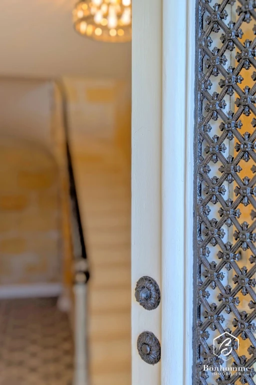 Porte en fer forgé ouverte, révélant un escalier intérieur lumineux.