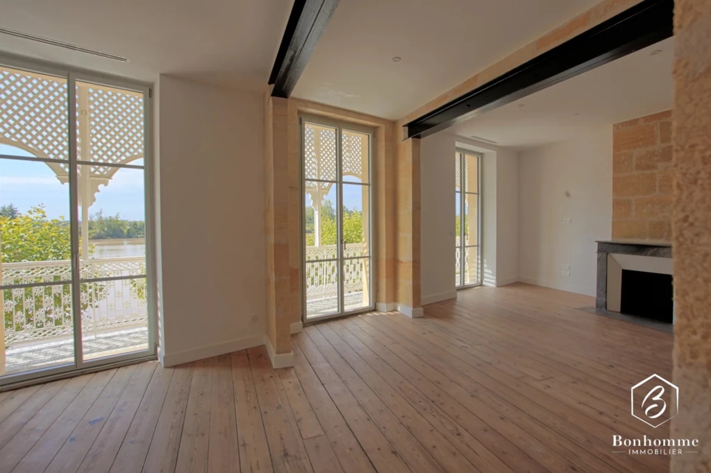 Une pièce lumineuse avec parquet, grandes fenêtres et cheminée.