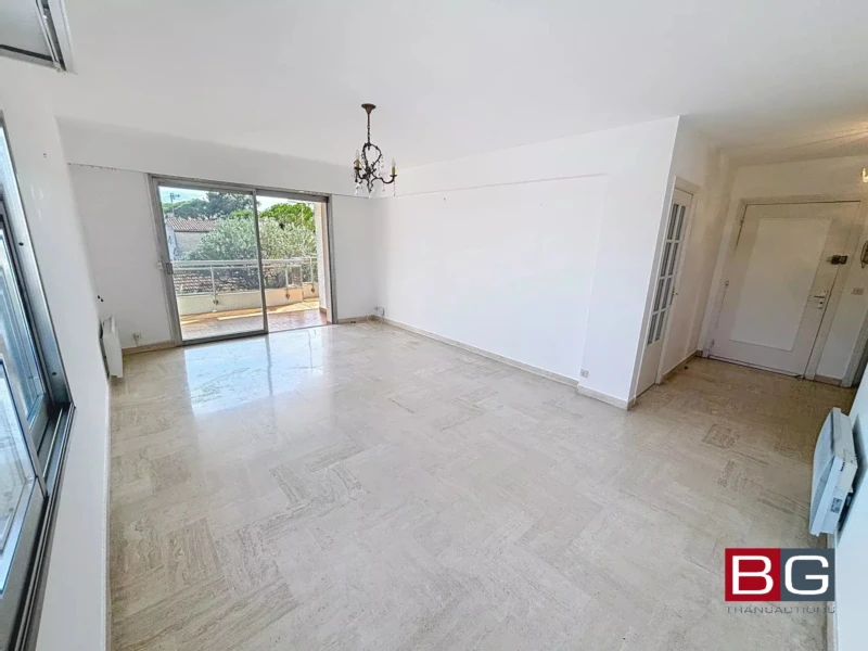 Une pièce lumineuse avec un sol en marbre et un lustre suspendu. Elle dispose d'une grande baie vitrée donnant sur un balcon. L'espace est clair et minimaliste.