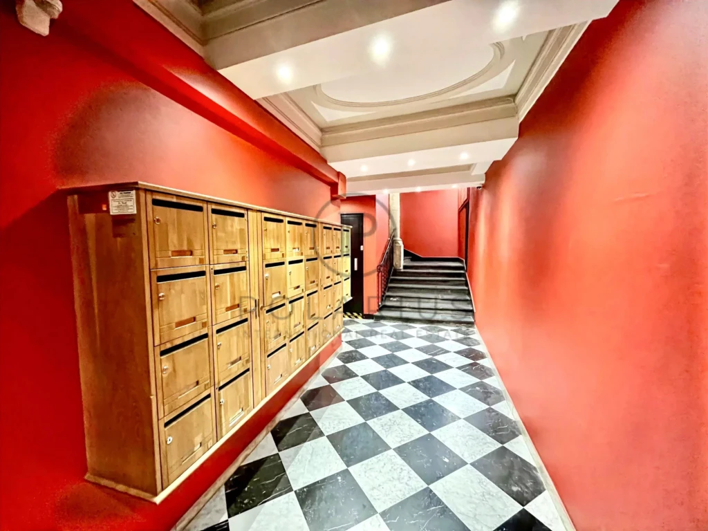 Couloir lumineux avec casiers en bois et sol en carreaux noirs et blancs.