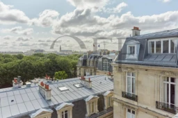 Vue sur les toits de Paris avec des bâtiments historiques et un ciel partiellement nuageux.