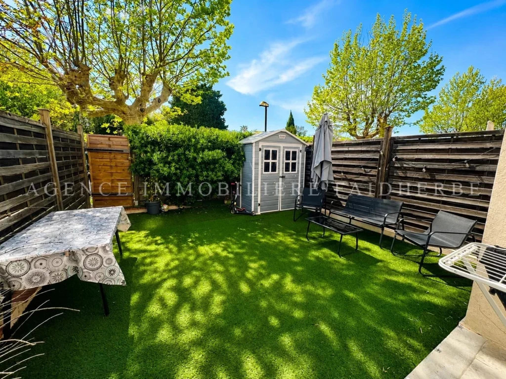 Jardin privé entouré d'une clôture en bois, avec un espace détente et un abri de jardin.