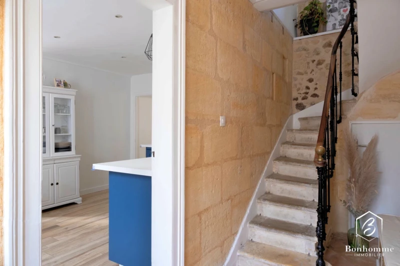 Un escalier en pierre avec une rampe en métal se trouve à côté d'une cuisine moderne et lumineuse.