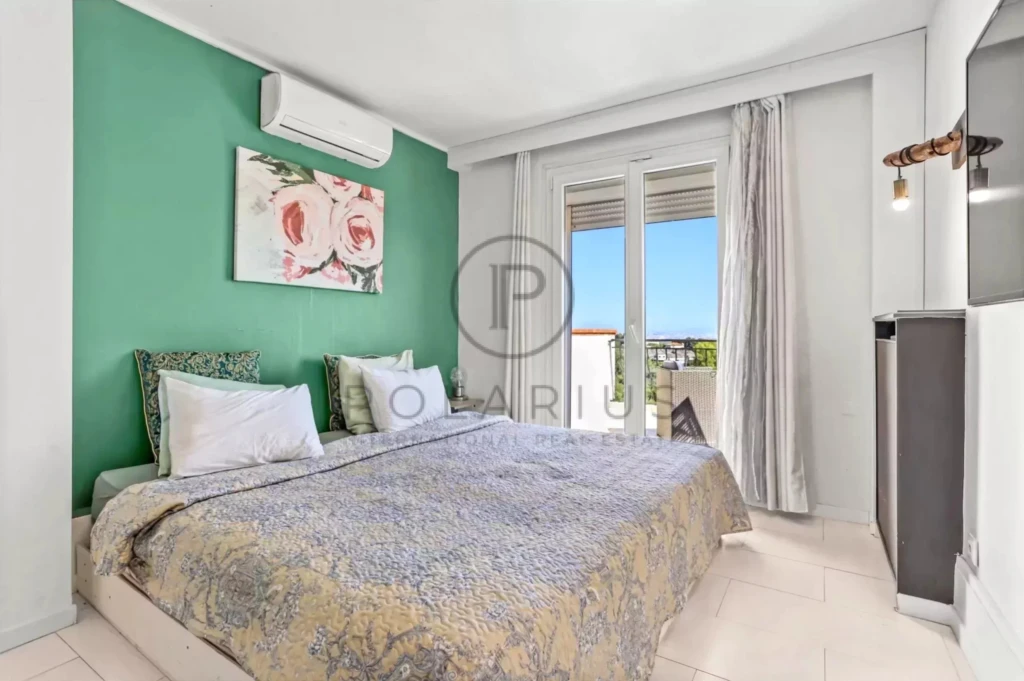 Une chambre lumineuse avec un mur vert, un lit double, une peinture florale et une grande fenêtre avec vue.