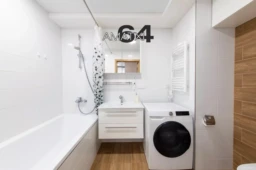 Bright and clean home bathroom featuring a bathtub, washing machine, sink, and wooden accents on the walls, combining functionality and aesthetic appeal in a compact space.