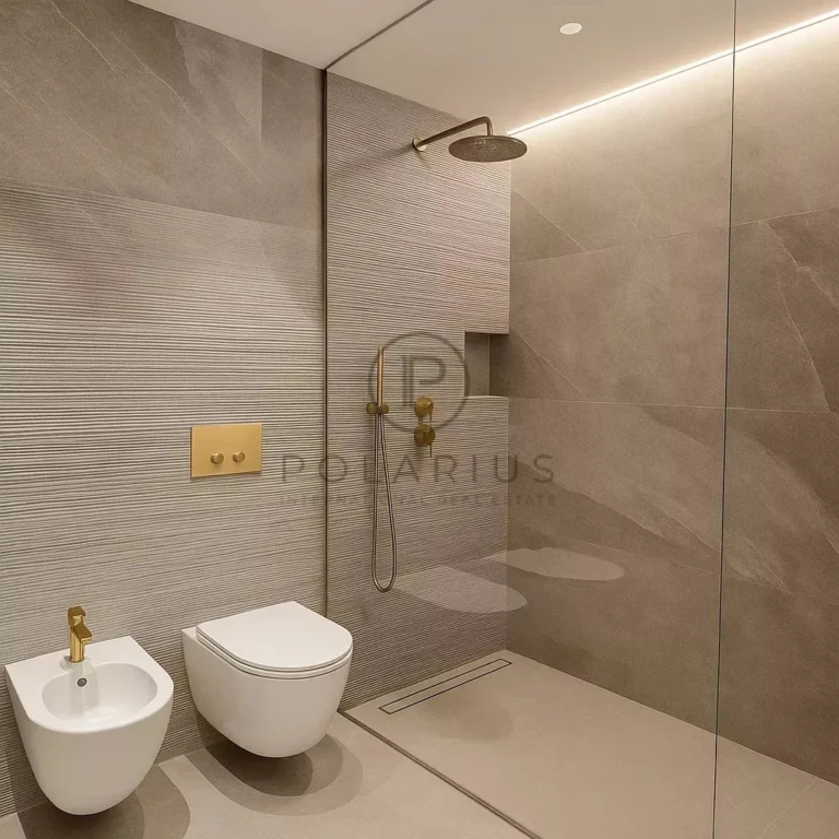 Une salle de bain moderne avec une douche à l'italienne, des toilettes et un bidet, des éléments dorés et des tons neutres.