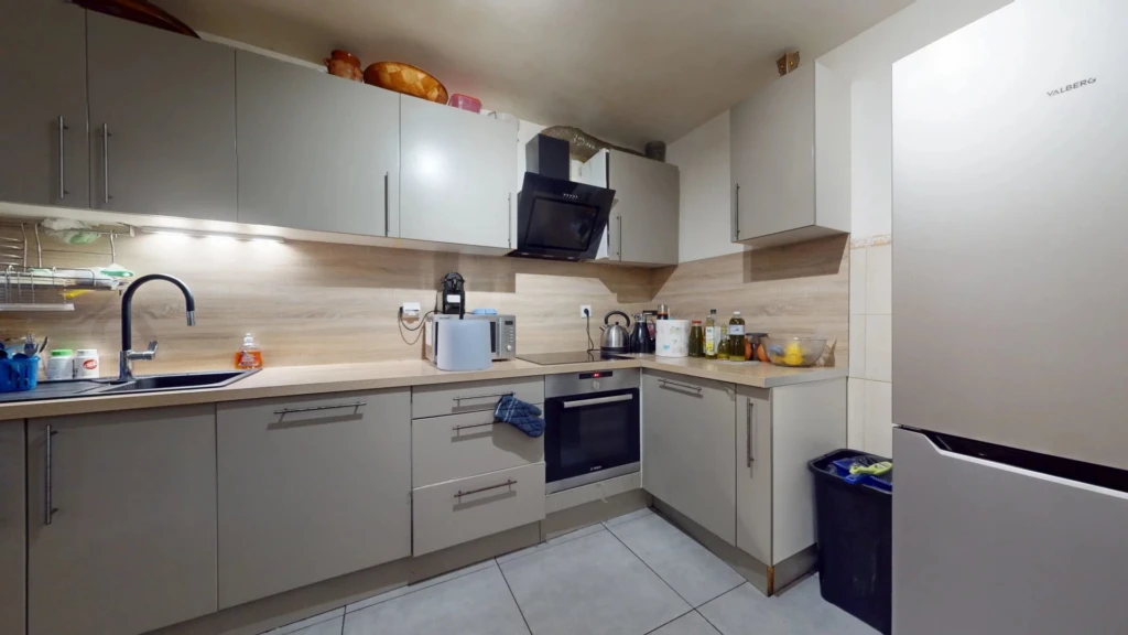 Cuisine moderne avec des armoires grises, plans de travail en bois clair, et des appareils électroménagers intégrés.