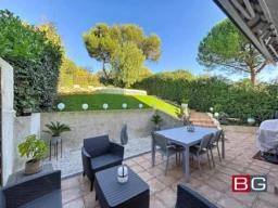 Une terrasse carrelée avec des meubles de jardin, entourée de verdure et éclairée par des lampes sphériques.