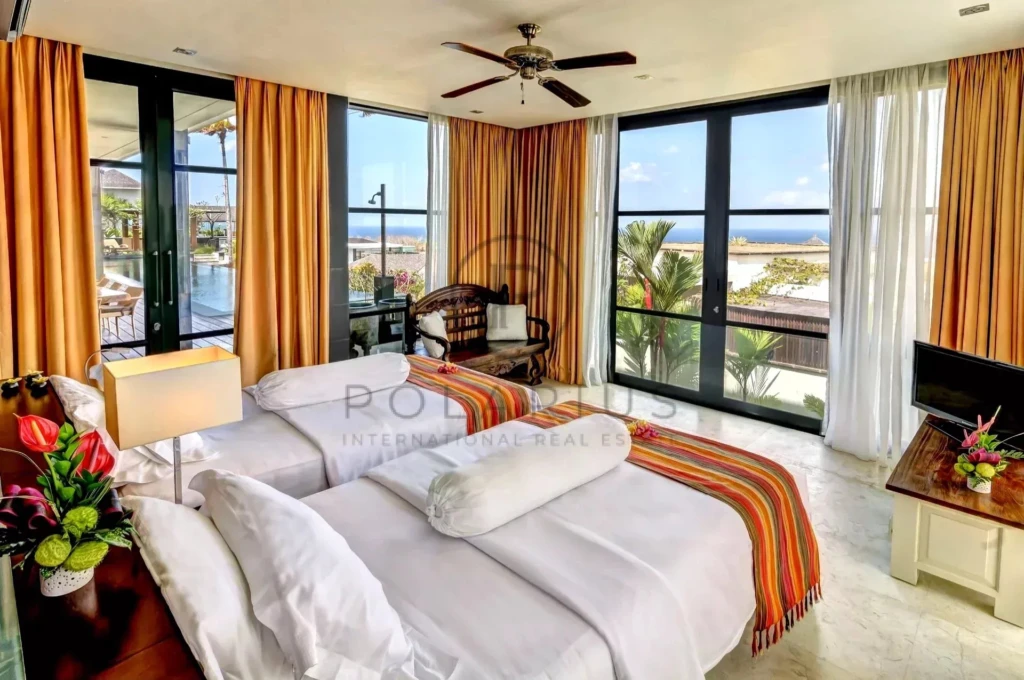 Une chambre lumineuse avec deux lits simples, des baies vitrées donnant sur une vue panoramique de la mer, décorée de plantes et de rideaux oranges.